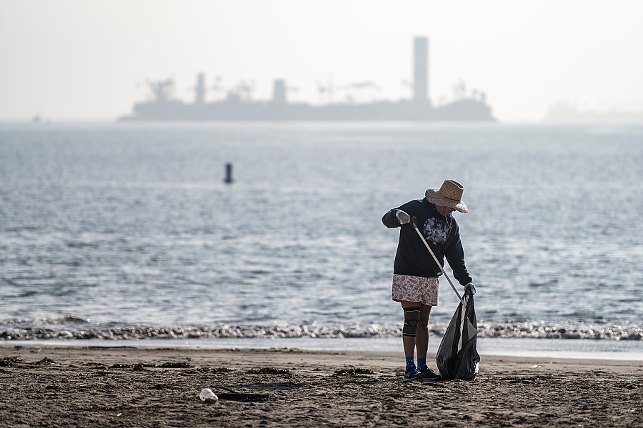 person on a beach carrying a trash bag and a reacher grabber